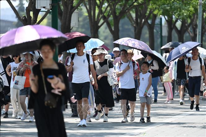 Người dân che ô tránh nắng khi di chuyển trên phố ở Bắc Kinh, Trung Quốc ngày 24/6/2023. Ảnh: AFP/TTXVN