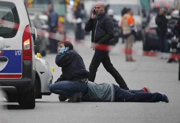 A police photographer (partially hidden) works with investigators as they examine the impacts from machine gun fire on the front of a police vehicle in the street near the Paris offices of Charlie Hebdo, a satirical newspaper, after a shooting January 7, 2015. Twelve people including two police officers were killed in a shooting at the Paris offices of the satirical weekly Charlie Hebdo on Wednesday, a police spokesman said in an update on the death toll. The French president described the shooting as without doubt a terrorist attack. REUTERS/Christian Hartmann (FRANCE - Tags: CRIME LAW MEDIA)
